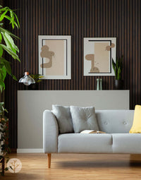 Gray sofa against smoked oak acoustic slat wood wall panels in a modern living room interior with minimalist artwork and plants.