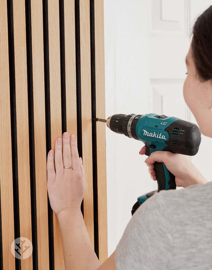 Person installing Natural Oak Acoustic Slat Wood Wall Panels with a drill for improved interior sound quality.