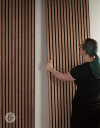 Person installing Natural Walnut Acoustic Slat Wall Panels for improved interior acoustics and elegance.