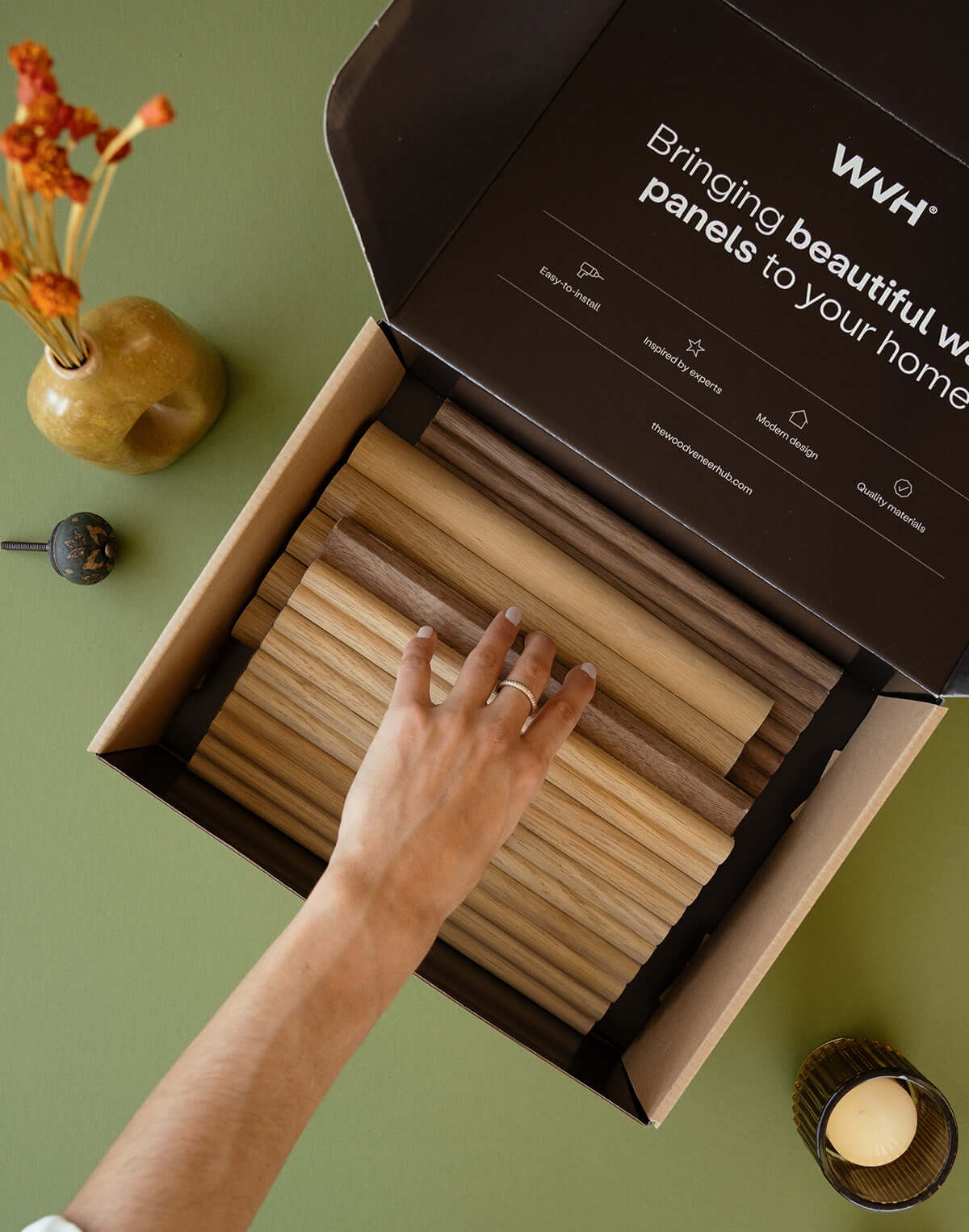 Flexible tambour wood panels sample box showcasing various wood finishes and a hand selecting a panel.