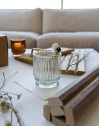 Clear glass candle holder on a table with wooden panels and decorative branches, creating a cozy atmosphere.