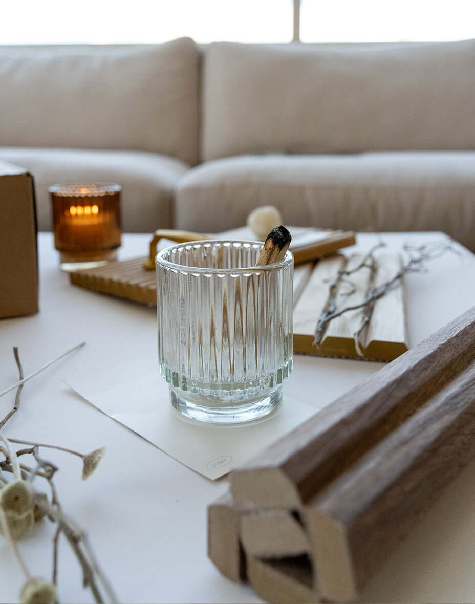 Clear glass candle holder on a table with wooden panels and decorative branches, creating a cozy atmosphere.