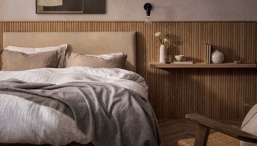 Cozy modern bedroom with beige headboard, wooden wall panel, and minimalist decor.