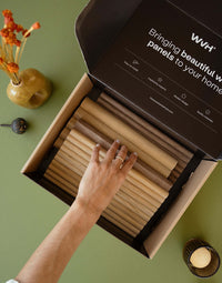 Flexible tambour wood panels sample box showcasing various wood finishes and a hand selecting a panel.